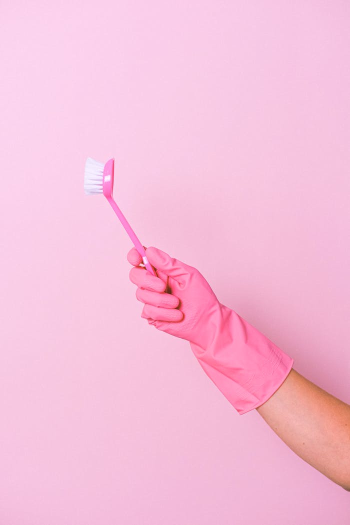 why-choose-us A person wearing a pink glove holds a cleaning brush against a pink background.